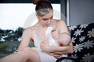 Young caring mother breastfeeding her little baby on grey house background
