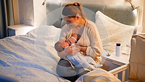 Young caring mother feeding her newborn baby son in dark room at night. Concept of healthy and natural baby nutrition