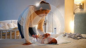 Young caring mother giving soother to her little baby boy crying on bed at night. Parent giving pacifier to newborn