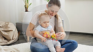 Young caring mother playing toys with her baby son on carpet in living room