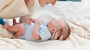 Young caring mother putting her little baby son on soft blanket in bedroom. Concept of family happiness and loving