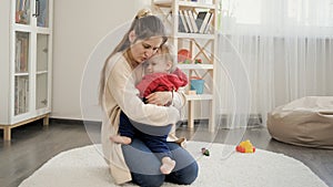 Young caring mother soothing and comforting her upset crying baby boy on carpet in living room