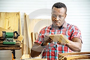 Young carpenter african american man looking and choosing wood and using sandpaper to rub wooden plank at workshop table in
