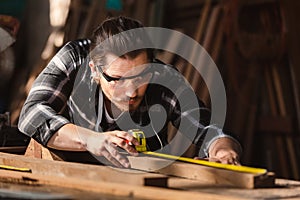 Young carpenter caucasian man using measuring tape looking wood size at workspace. craftsman profession in wood factory