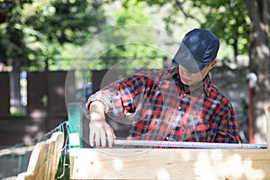 Young carpenter measuring wood using a tape measure in the garden