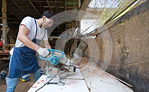 Young carpentry using a power miter saw to cut a piece of wood. Atmosphere in a workshop or outdoor shed based on the rustic