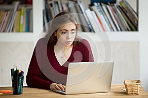 Young casual businesswoman staring at laptop screen with surpris