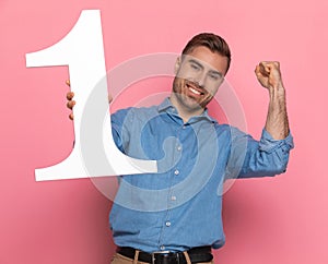 Young casual guy in denim shirt holding number one