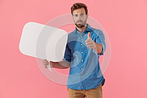 Young casual guy holding speech bubble and making thumbs up sign