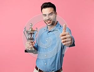 Young casual guy holding trophy and making thumbs up sign