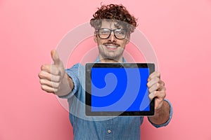 Young casual guy making thumbs up sign and presenting tab