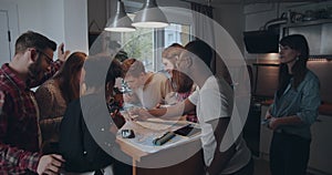 Young casual happy multiethnic student friends using big map on kitchen table with pencils planning travel slow motion.