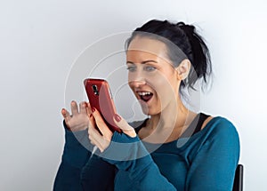 Young casual hipster woman holding and looking at cell phone reading unexpected sms news with a surprised facial expression