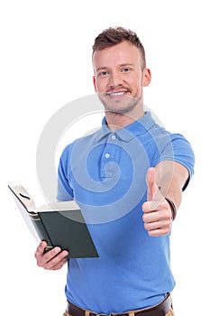 Young casual man with book shows thumb up