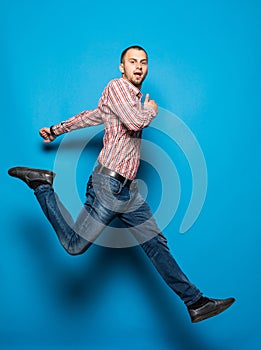 Young casual man jumping for joy on blue background