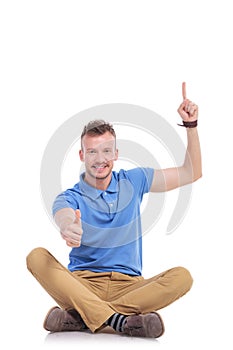 Young casual man points up and gives thumb up