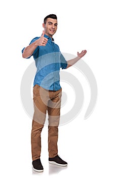Young casual man presents to side and makes ok sign
