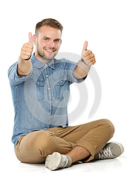 young casual man sitting with legs crossed and showing both thumbs up to the camera, smile