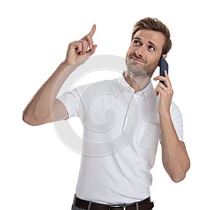 Young casual man talking on the phone is pointing up