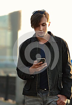 Young casual man walking on the street and chating on mobile phone holding in the hand on city center background