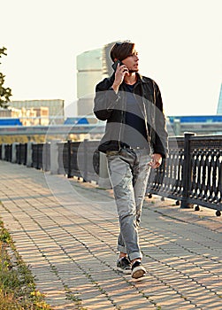 Young casual man walking on the street and talking on mobile phone on city center background