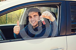 Young casual man wearing blue shirt holding car keys out of the window, showing thumb up positive gesture