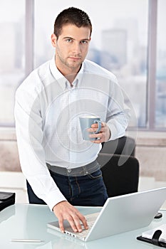 Young casual office worker using laptop in office
