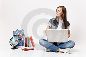 Young casual smart woman student holding using laptop pc computer looking aside sitting near globe, backpack, school