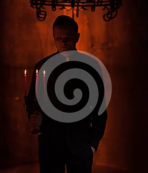 Young Catholic Praying priest. Portrait of priest Next to the candles prays with his hands folded near the face.