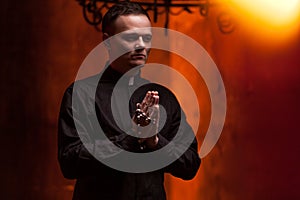 Young Catholic Praying priest. Portrait of priest Next to the candles prays with his hands