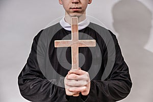 A young Catholic priest holds a cross in front of him. The concept of driving out the devil and evil spirits