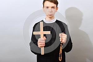 A young Catholic priest holds a cross and a rosary in his hand