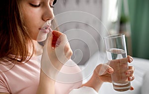 Young Cauasian woman with glass of water taking pill, not feeling well, using medications at home. Health care concept photo