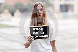 Young caucasian activist woman holding banner with inscription Stop hating russians