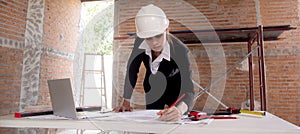 Young caucasian architect woman looking laptop and working drawing blueprint for planning building house.