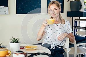 Young caucasian attractive smiling blonde is drinking coffee in a coffee shop.