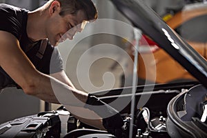 Young caucasian auto mechanic in a car service, checks a car, engine, carburetor
