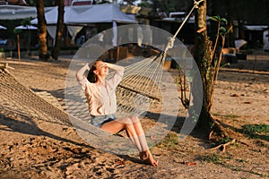 Young caucasian barefoot girl resting on sand in white wicker hammock.