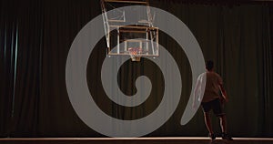 Young Caucasian basketball player plays throwing the ball into the basket. Winner night evening sports hall parquet