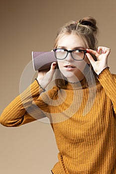 Young Caucasian Blond Girl Listening To Arcane Hidden Gossips and Secrets Using Disposable paper Drinking Cup Over Beige