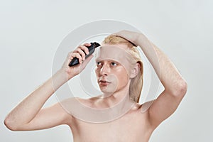 Young caucasian blond man using hair trimmer