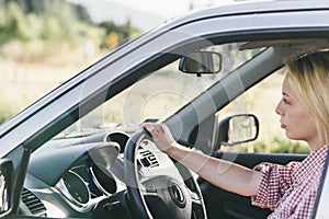 Young caucasian blond woman traveling by car and having fun on her summer holiday journey. Happy girl driving car on countryside