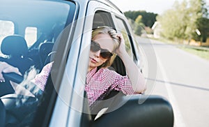 Young caucasian blond woman traveling by car and having fun on her summer holiday journey. Happy girl driving car on countryside