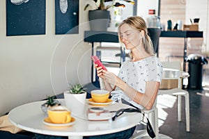 A young caucasian blonde sitting in a coffee shop. Woman laughing while communicating in mobile