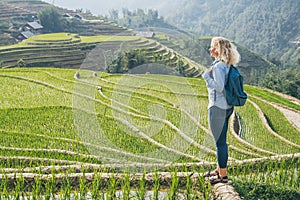 Young Caucasian blonde woman in denim shirt overlooking Sapa rice terraces at sunset in Lao Cai province, Vietnam