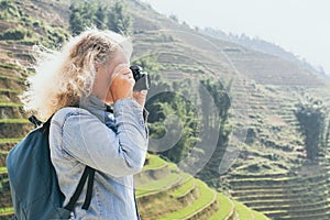 Young Caucasian blonde woman in denim shirt taking pictures of Sapa rice terraces at sunset in Lao Cai province, Vietnam