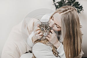 Young caucasian blonde woman hugging and kissing her brown tabby cat