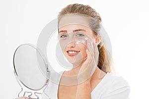 Young caucasian blonde woman with mirror and face skin care moisturizing cream on face isolated on white background. Anti aging