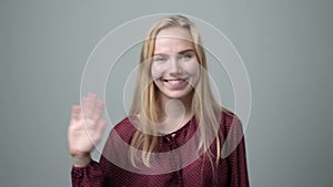 Young caucasian blonde woman waving hand, welcoming her friend.