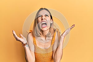 Young caucasian blonde woman wearing casual yellow t shirt crazy and mad shouting and yelling with aggressive expression and arms